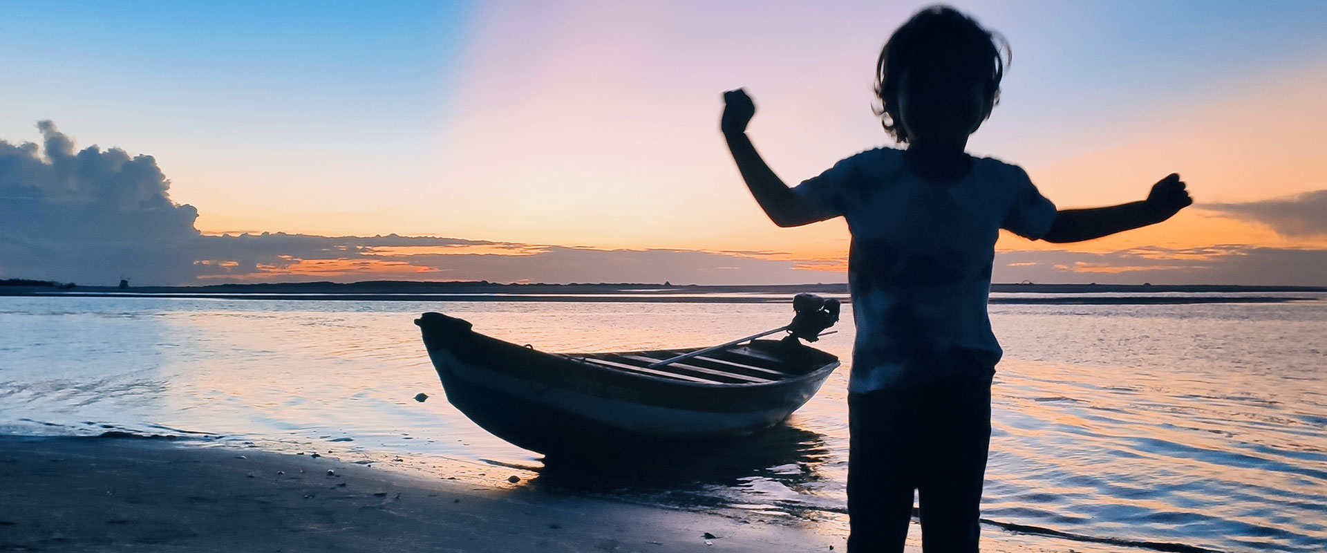 A kid enjoying the sunset on a beach next to a boat in Atins