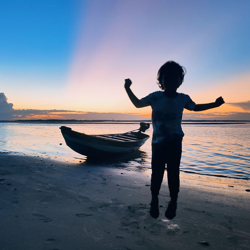 A kid enjoying the sunset on a beach next to a boat in Atins