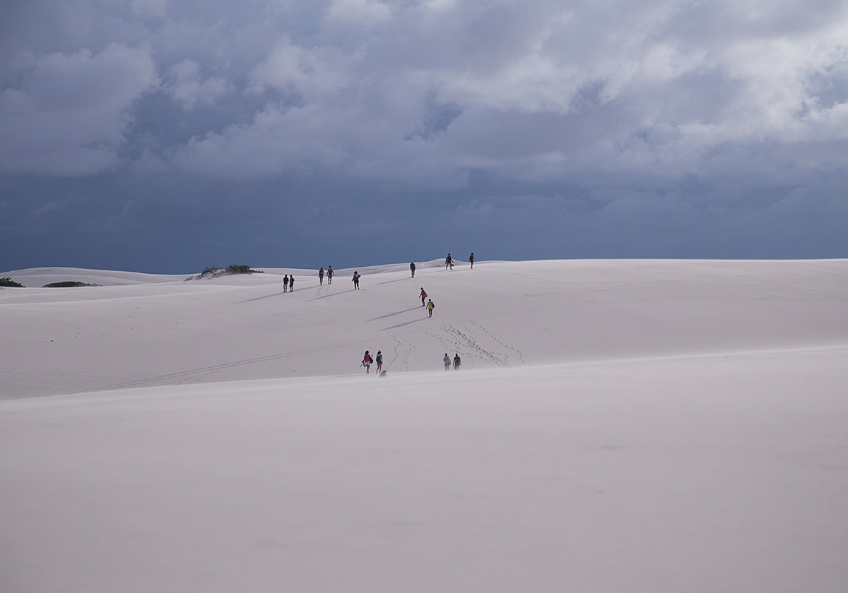 A group of people walking across the sand dunes in Lençóis Maranhenses