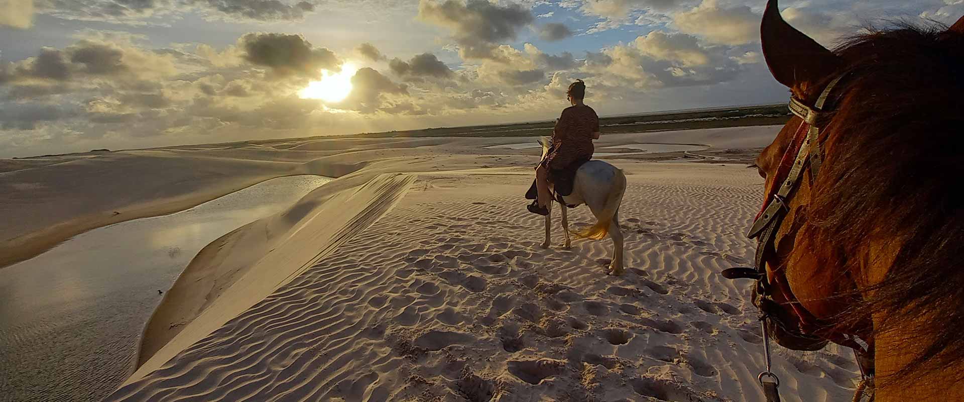A person horseback riding on the sand dunes of Lençóis Maranhenses at sunset