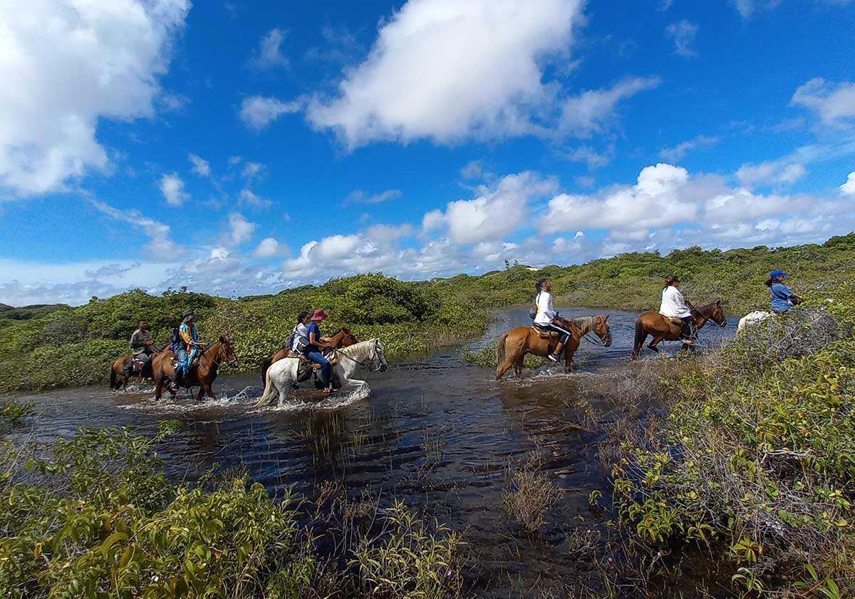 A group of people horseback riding across a river in Lençóis Maranhenses
