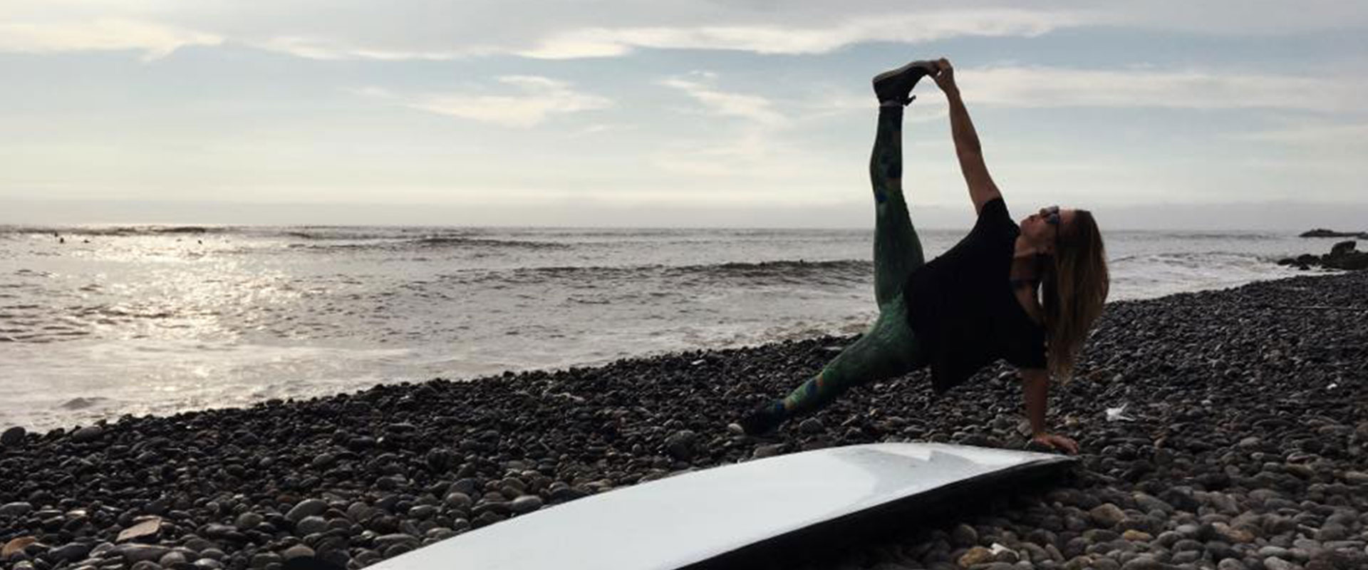 A person doing a yoga pose on the beach behind a surf board