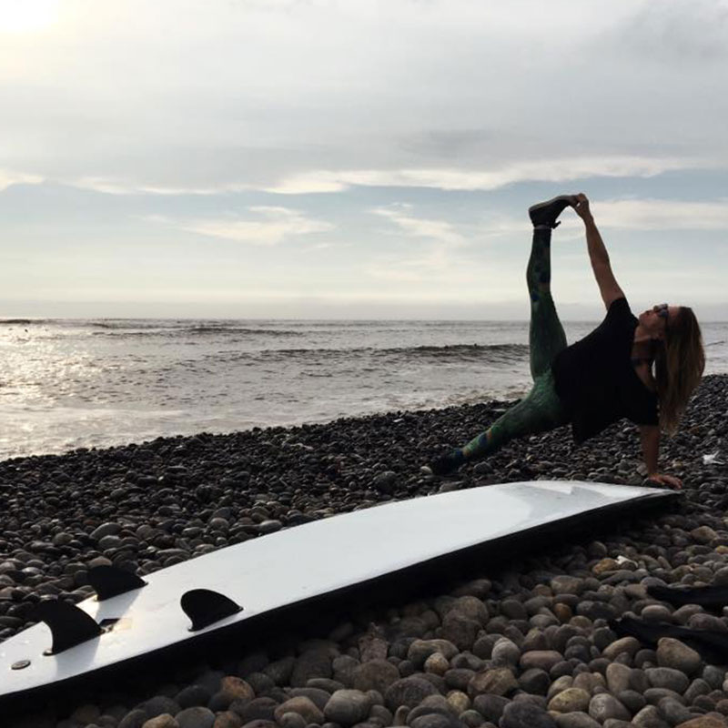 A person doing a yoga pose on the beach behind a surf board